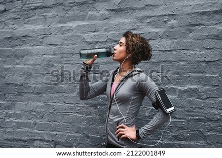 Hydrate and replace those electrolytes. Cropped shot of an attractive young woman listening to music and drinking water after working out while outside.