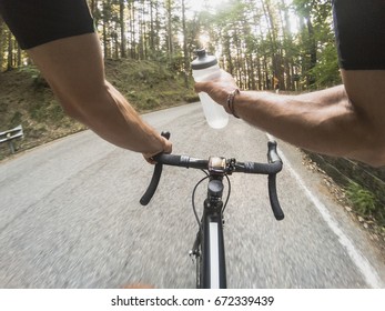 Hydrating On A Racing Bicycle. Personal Perspective. Pov Shot Of A Young Adult Man Drinking From A Water Bottle While Riding A Bicycle At Sunset. Sun Flare Enhanced.