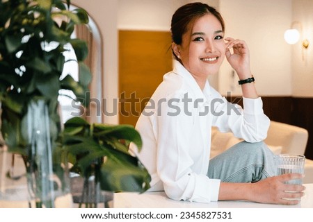 Hydration concept. Young attractive asian woman drinking spring water at home, looking at copy space. Beautiful lady holding glass of mineral water, hydrating her body in the morning