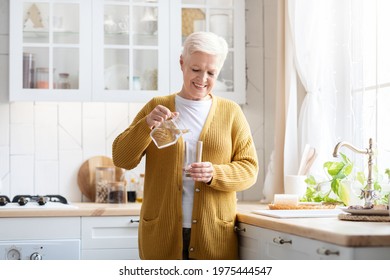 Hydration, Healthy Lifestyle Cocnept. Smiling Senior Woman Pouring Water Into Glass, Kitchen Interior. Attractive Older Woman In Casual Outfit Holding Glass Of Fresh Water, Copy Space