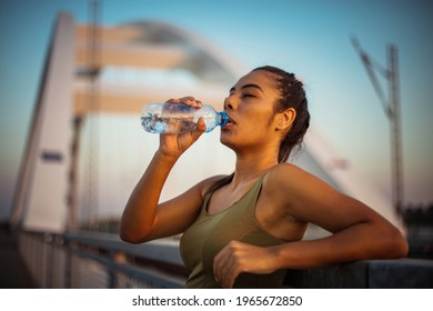 Hydration. Sports young woman standing on the bridge and drinking water after exercise.  - Powered by Shutterstock