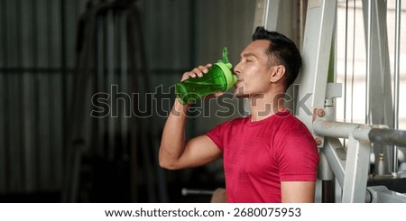 Hydration. Young man drinking from shaker bottle after workout in gym.
