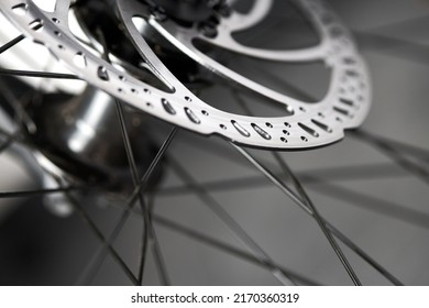 Hydraulic bicycle disk brakes, grey metal disc attached to bike wheel close up, effective popular mountain bicycle brakes. Hydraulic disk brakes on bicycle wheel, bicycle spokes gray background