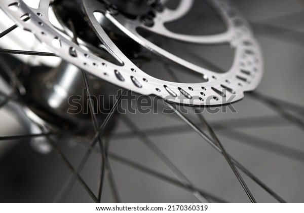 Hydraulic bicycle disk brakes, grey metal disc\
attached to bike wheel close up, effective popular mountain bicycle\
brakes. Hydraulic disk brakes on bicycle wheel, bicycle spokes gray\
background