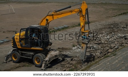Hydraulic breaker hammer excavator at demolition work. yellow crusher excavator stands sideways on ruins of building against backdrop of rural landscape and blue sky Crushing concrete structures