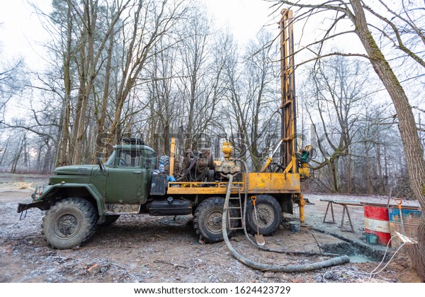 Hydraulic ground water hole drilling machine\
installed on the old truck with big wheels on the construction\
site. Groundwater well\
drilling.