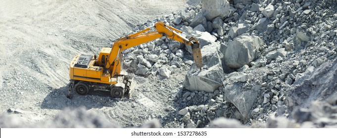 Hydraulic hammer works in a quarry against the background of huge gray stones, panorama.