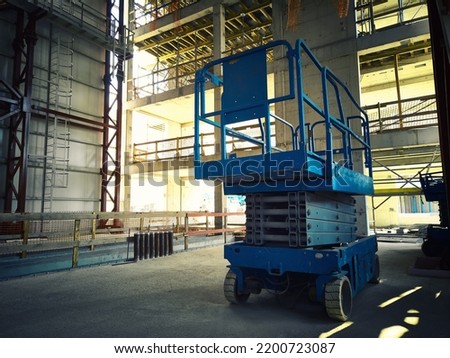 Hydraulic lifting platform at construction site. Scissor lift platform inside of industrial building. Cherry picker or aerial manlift
