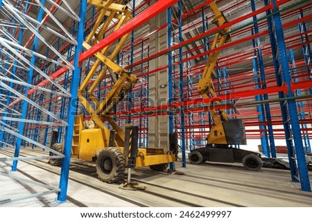 Hydraulic lifting platform on the construction site of an industrial building. A scissor elevator inside a huge warehouse is used to install tall metal shelving units