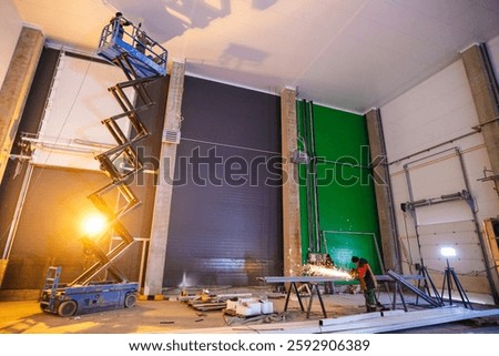 Hydraulic lifting platform on the construction site of an industrial building. The scissor lift inside the huge warehouse is used to work at height