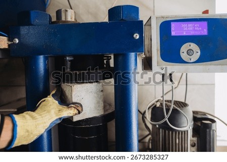 Hydraulic press machine testing compression strength of concrete cube sample in material testing laboratory, determining its resistance to compression stress