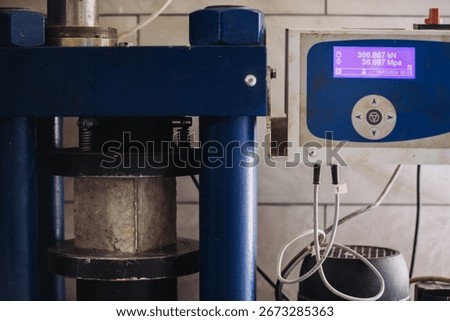 Hydraulic press performing compression test on concrete sample in material testing laboratory, checking its resistance and quality