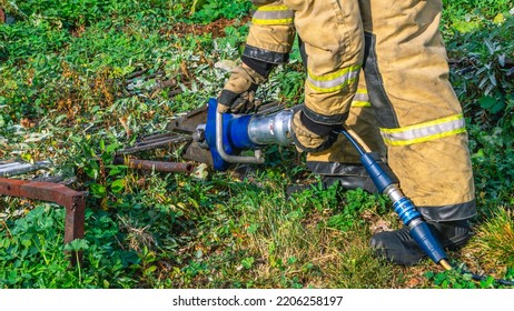 Hydraulic Scissors For Emergency Rescue Operations. Manual Mechanized Tool. A Firefighter In Special Protective Clothing And Mittens Cuts Metal Bars With Hydraulic Scissors To Prevent Injuries.