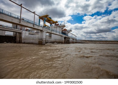 Hydro Technic Construction. Shardara River Dam Near Kazaly City. Overhead Crane On Bridge. Blue Sky With White Clouds. Yellow River Water. Kyzylorda Region, Kazakhstan.