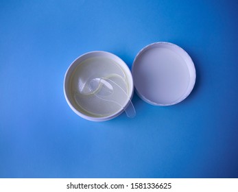 Hydrogel eye patch in a white jar with special spatula. Pack of under-eye masks for reducing dark circles, puffiness and fine lines top view on blue background. Beauty skin care for women and men.