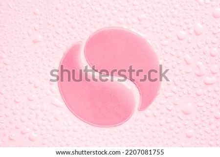 Hydrogel pink eye patches on pink background with water drops close up. Cosmetic moisturizing under eye patches with collagen.