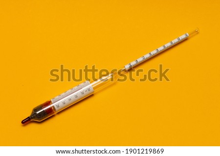 A hydrometer is a device for measuring the density of liquids and solids. Yellow background. Close-up.