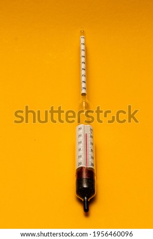 A hydrometer is a device for measuring the density of liquids and solids. Close-up. Yellow background.