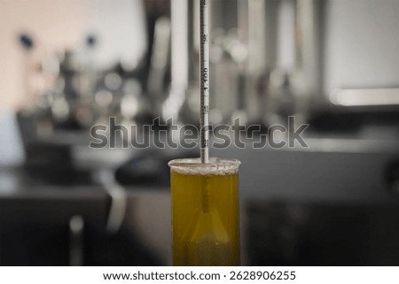 Hydrometer floating in a yellow liquid inside a graduated cylinder, used for measuring specific gravity in a laboratory setting