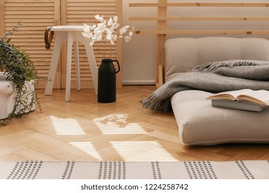 Hygge Bedroom With Scandinavian Futon As A Bed Next To White Flowers In Black Vase And Wooden Coffee Table, Real Photo