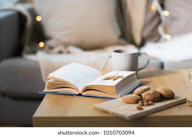 Hygge And Cozy Home Concept - Book With Autumn Leaf, Cup Of Tea And Oatmeal Cookies On Wooden Table