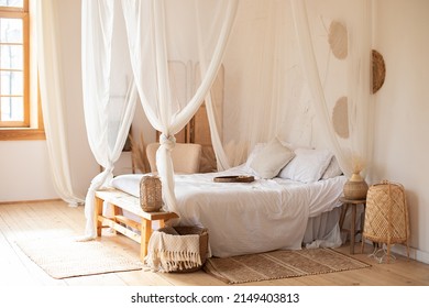 hygge decor at home. interior white bedroom in boho  style with coffe table,straw lamp and comfortable bed with pillows, copy space. bed with flowing white curtains. Cozy scandinavian decoration room