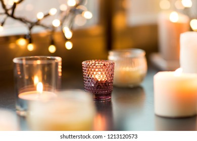 hygge, decoration and christmas concept - candles burning in lanterns and festive garland on window sill at home