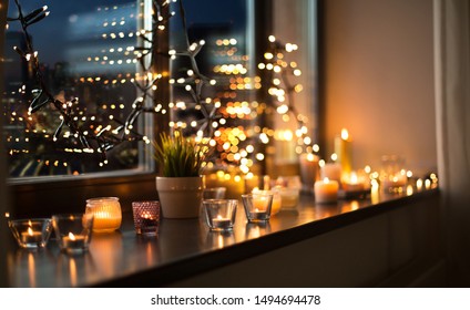 Hygge, Decoration And Christmas Concept - Candles Burning In Lanterns On Window Sill And Festive Garland String At Home