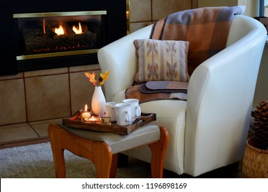 Hygge Home Comfort With Soft Leather Bucket Chair, Candles, Blanket And Tea Beside Gas Fireplace.  Horizontal Format In Natural Light