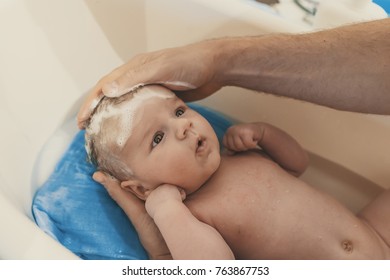 Hygiene and care for baby. Unrecognizable father bathing her son in white small plastic bat. Portrait of a baby is being bathed by his father. Soft tone. Bath time for a cute little newborn baby