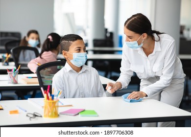 Hygiene And Cleaning. Teacher cleaning table with antibacterial sanitizer and napkin, disinfecting surface, applying antiseptic spray on desk, wearing disposable face mask, boy studying in classroom - Powered by Shutterstock