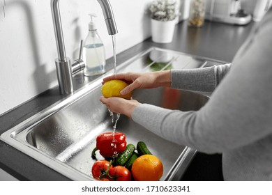 hygiene, health care and safety concept - close up of woman washing fruits and vegetables in kitchen at home