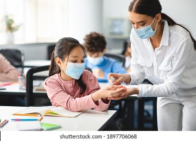 Hygiene And Healthcare Concept. Teacher Applying Antibacterial Sanitizer Spray On Asian Schoolgirl's Hands, Wearing Disposable Face Mask, Studying In Classroom At School. Prevent Spread Of Infection