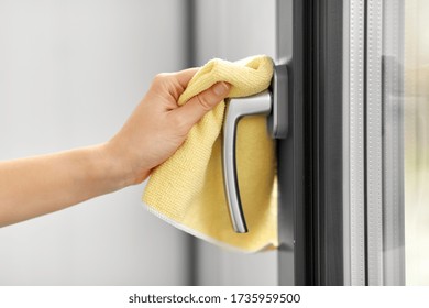 hygiene, household and cleanliness concept - close up of female hand cleaning window handle with microfiber rag