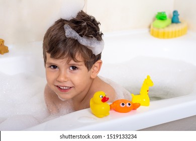 Hygiene for infant and baby. Child playing with soap foam in home bathroom. Rubber duck in foam bath 
