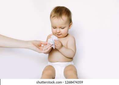 Hygiene - young momy wiping the baby skin with wet wipes. Little baby girl in diaper sitting and taking the wet wipe from mother hand. Cleaning wipe, pure, clean