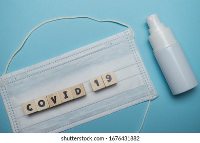 Hygienic face mask and white bottle hand sanitizer with covid-19 word written on wood block isolated over blue background. Virus outbreak prevention concept.