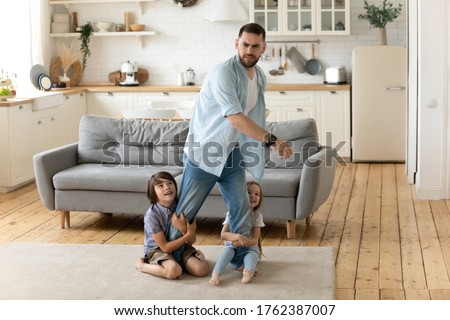 Hyperactive kids holding tired upset father legs when they want to relax. Frustrating dad stressful feels heaviness and headache at home. Fatigue man does n't not want to play with son and daughter. Foto stock © 