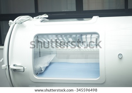 Hyperbaric Oxygen Therapy (HBOT) chamber tank used for specialised medical treatment for injuries in hospital clinic. Exterior viewing window and pressure dial gauge with pillow and bed inside. 