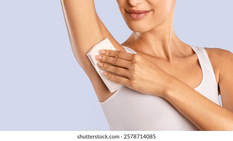Hyperhidrosis Concept. Closeup cropped view of young lady wiping her under arm area with napkin towel, rubbing armpit isolated on blue studuo background, putting hand up, touching axilla. Perspiration