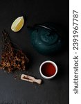 Hypericum Perforatum Herbal Tea In Teapot And small teacup and piace of lemon On Black Background. Low Key. Flat Lay. Vertical orientation.