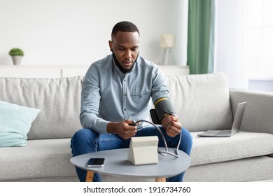 Hypertension. African Man Measuring Arterial Blood Pressure Having Health Problem Sitting On Sofa At Home. Hypotension And High Pressure Issue Concept. Selective Focus