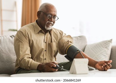 Hypertension In Older Age. Senior Black Man Measuring Arterial Blood Pressure Having Problems With Tension, Using Blood-Pressure Cuff Sitting On Sofa At Home. Healthcare And Medicine Concept