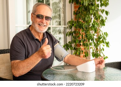 Hypertension In Older Age. Senior Caucasian Man Measuring Arterial Blood Pressure Sitting On Sofa In The Terrace At Home. Healthcare And Medicine Concept