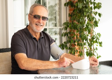 Hypertension In Older Age. Senior Caucasian Man Measuring Arterial Blood Pressure Sitting On Sofa In The Terrace At Home. Healthcare And Medicine Concept