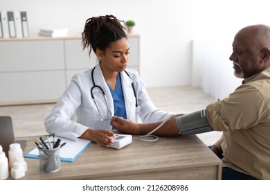 Hypertension In Older Age. Young Female Medical Worker Measuring Arterial Blood Pressure Of Senior Black Man Using Cuff, Patient Having Problems With Tension, Sitting At Table. Health Care Concept