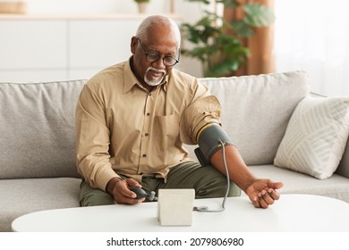 Hypertension Problem In Senior Age. African American Man Measuring Arterial Blood Pressure Using Sphygmomanometer Cuff Sitting On Couch At Home. Healthcare, Health Issue