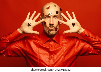 Hypnotizing Man Concept. Handsome Young Bald 40 Years Old Man With Confetti Stars On His Face Dancing And Looking Happy, Funny Over Scarlet Background. Copy-space. Studio Shot