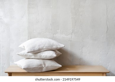 Hypoallergenic pillows in natural pillowcases lying on wooden bench in bedroom. Cushions on living room shelf against copy space background. Laundry day, cotton bedding and cleaning service concept