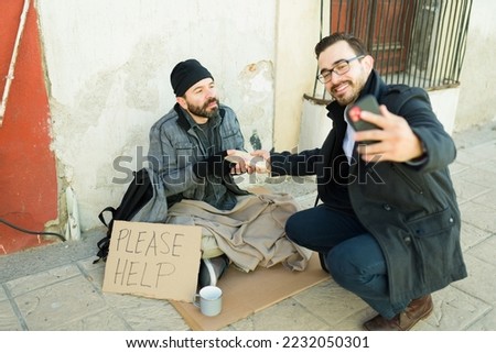 Hypocrite man doing charity and giving food to a homeless beggar man while taking advantage and taking a selfie